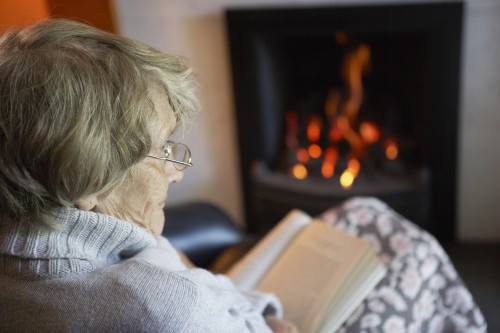 Senior Woman Reading Book By Fire At Home